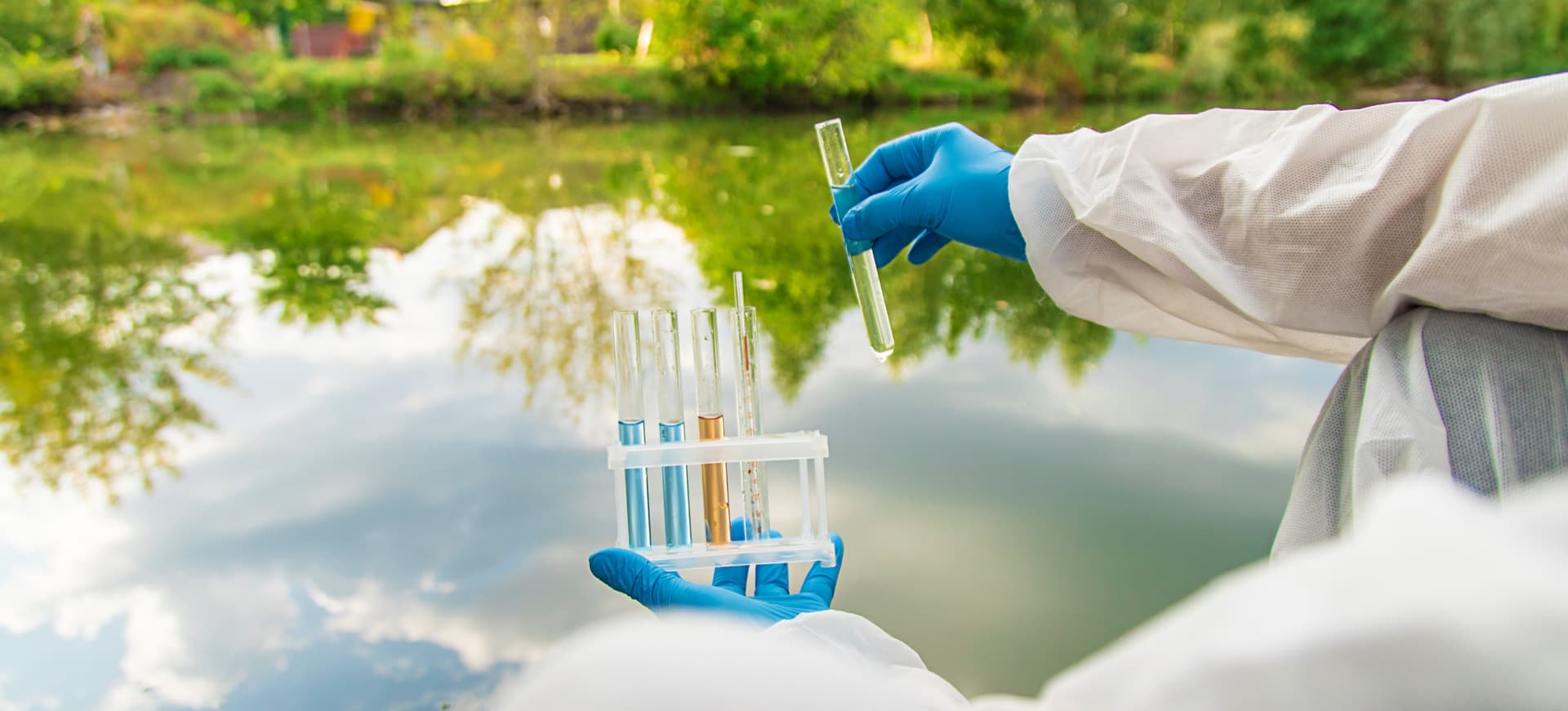 Scientist holding water samples beside a tree-lined river